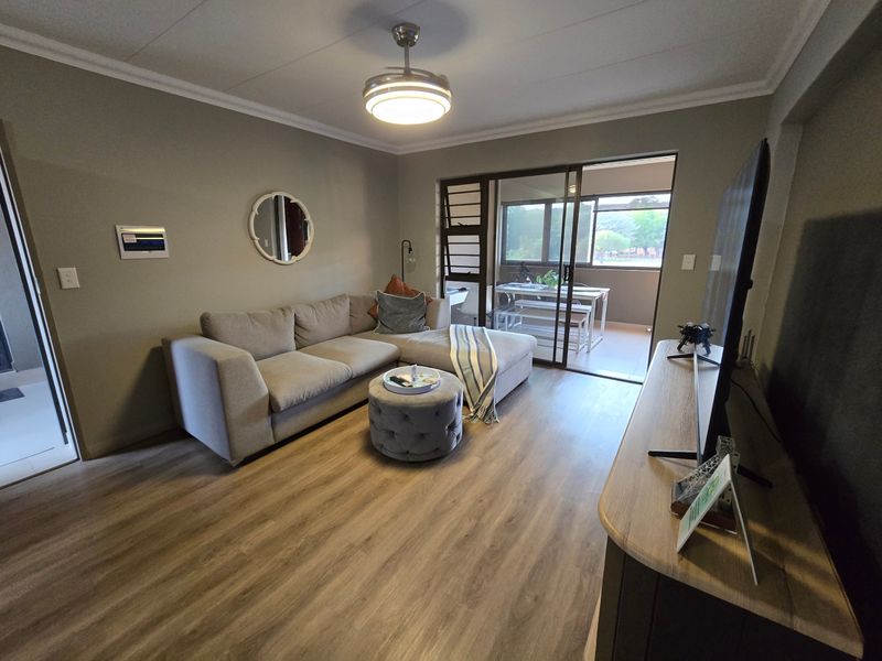 A well-maintained living room featuring modern laminate flooring, a ceiling fan, and a sliding glass door providing access to an outdoor patio area.