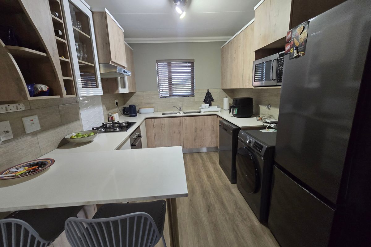 Modern kitchen featuring light wood-tone cabinetry, stone-look countertops, gas hob, built-in oven, and integrated microwave with a functional breakfast bar area.
