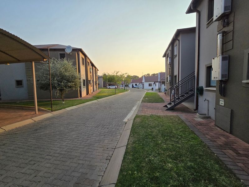 A view of a residential complex street featuring paved driveways, manicured lawns, external staircases, and modern building exteriors.