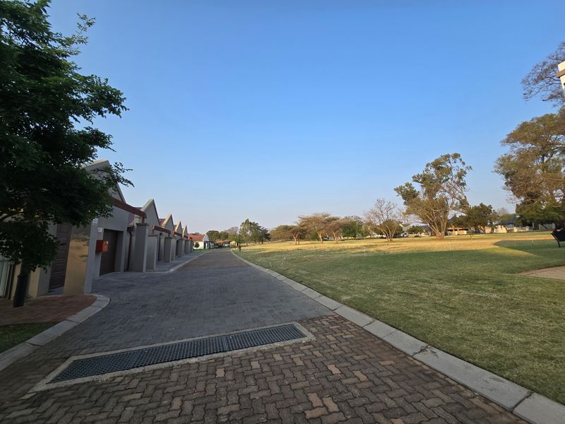 A view of the property's paved driveway and garage row, adjacent to a well-maintained open lawn area within the estate.