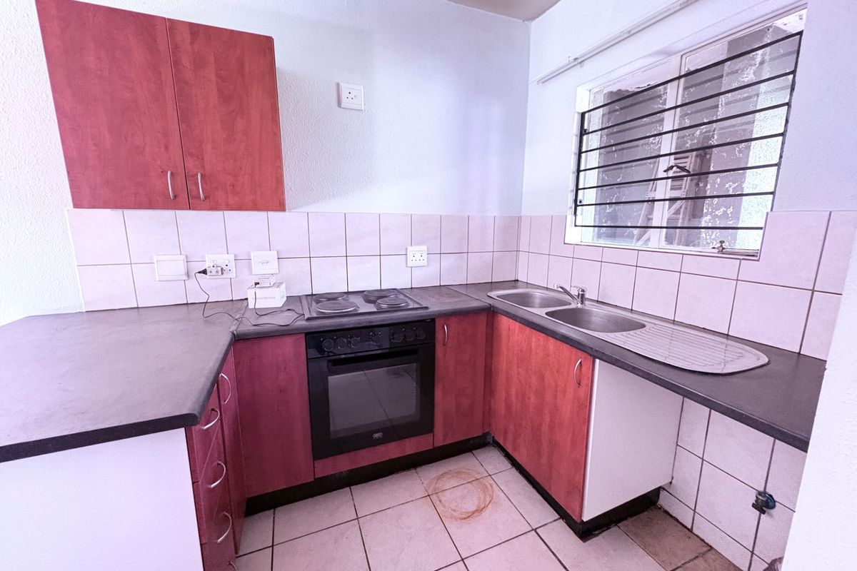 A functional kitchen featuring built-in cabinetry, a stainless steel sink, and an integrated oven with hob, requiring some cosmetic updates to the finishes.
