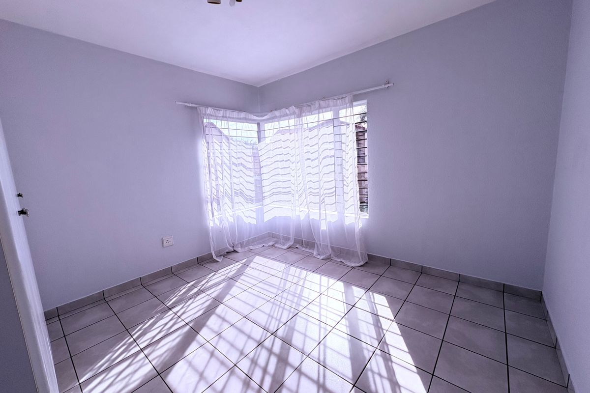 A bright, empty bedroom featuring neutral tiled flooring and a corner window with natural light.