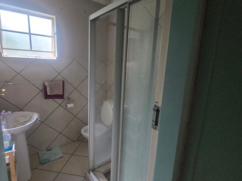 A compact bathroom featuring a pedestal basin, toilet, and shower enclosure, currently showing signs of ceiling water damage and dated finishes.