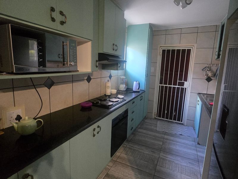 A functional galley-style kitchen featuring light-colored cabinetry, dark granite countertops, built-in oven and hob, and tiled flooring with direct access to the exterior.