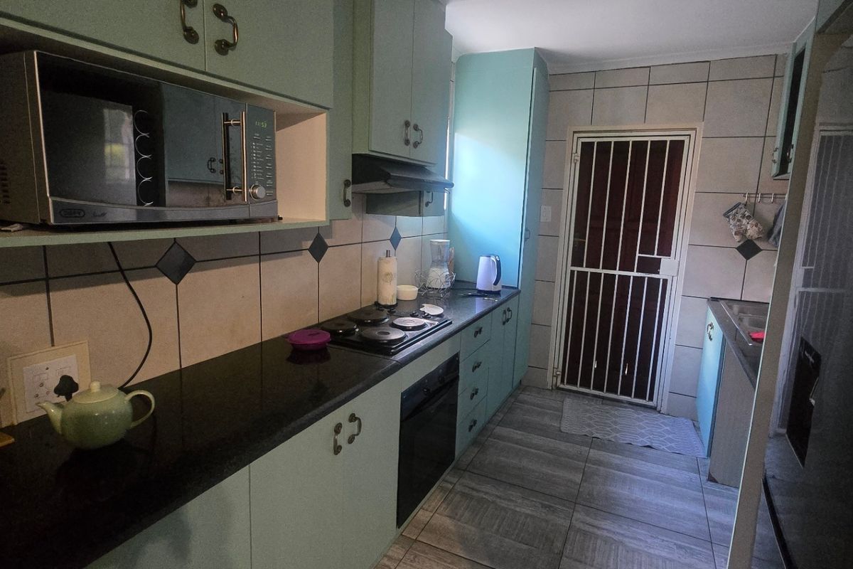 A functional galley-style kitchen featuring light-colored cabinetry, dark granite countertops, built-in oven and hob, and tiled flooring with direct access to the exterior.