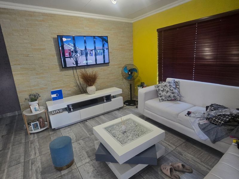 A well-maintained living room featuring a stone veneer accent wall, tiled flooring, and wooden venetian blinds, creating a bright and modern living space.