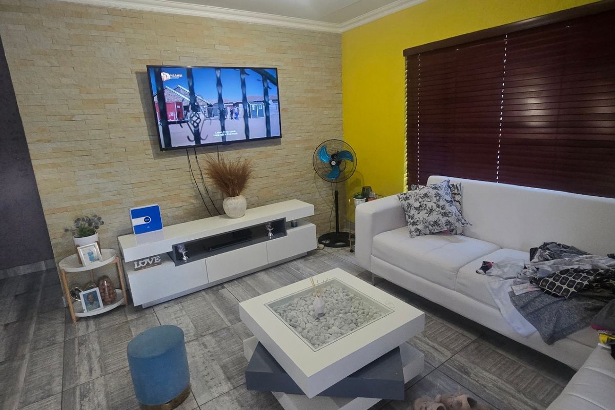 A well-maintained living room featuring a stone veneer accent wall, tiled flooring, and wooden venetian blinds, creating a bright and modern living space.