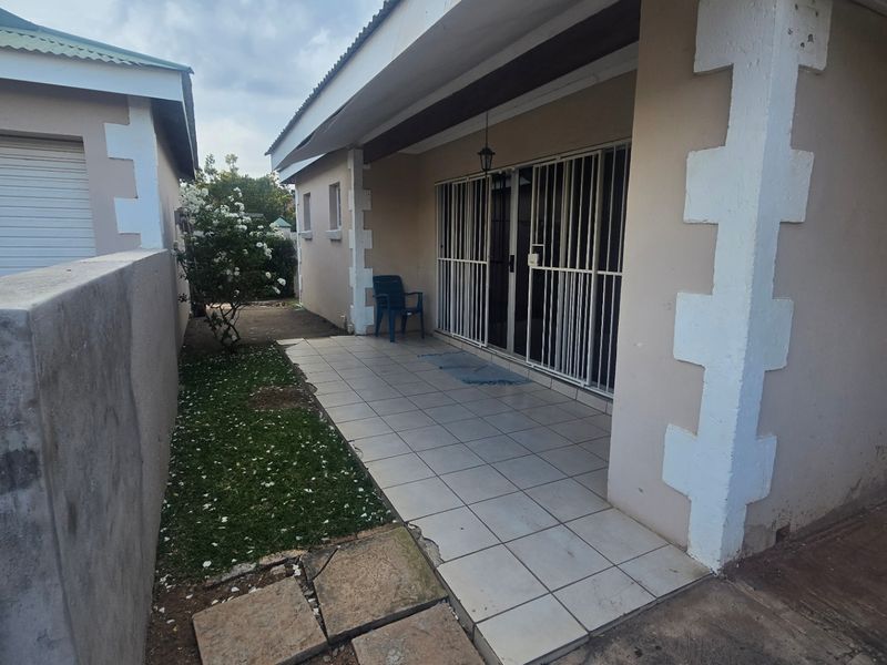A covered patio area featuring tiled flooring and security gates, adjacent to a small garden space and concrete boundary wall.