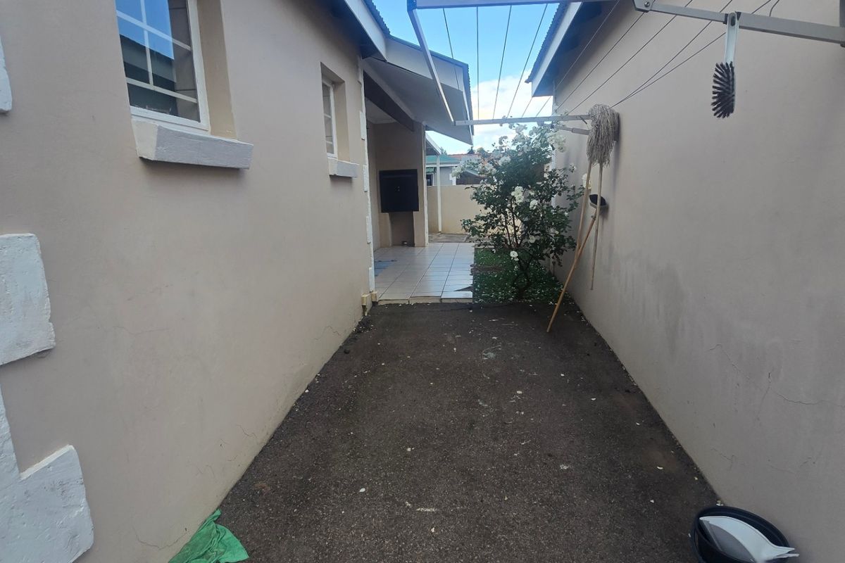 A narrow exterior side passage featuring a wall-mounted clothesline and access to a small tiled patio area at the rear of the townhouse.