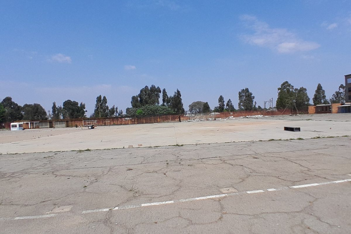 A large, vacant residential plot featuring extensive cracked concrete paving and perimeter fencing, offering a blank canvas for future development.