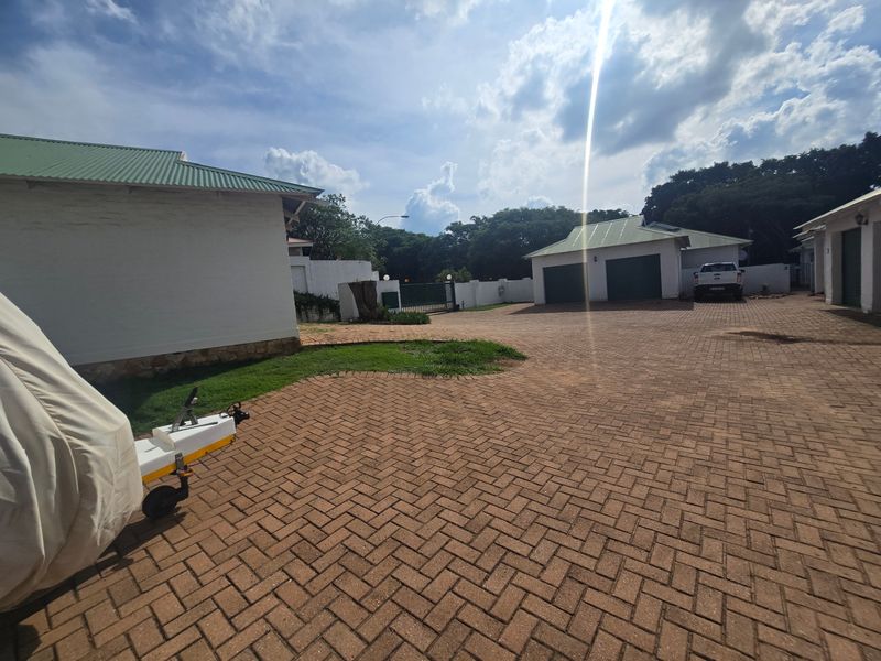 Spacious paved driveway leading to multiple garage units and the main property entrance, featuring well-maintained exterior structures and perimeter walling.