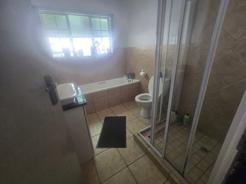 A functional bathroom featuring a bathtub, separate shower enclosure, toilet, and vanity basin with neutral tiled finishes.