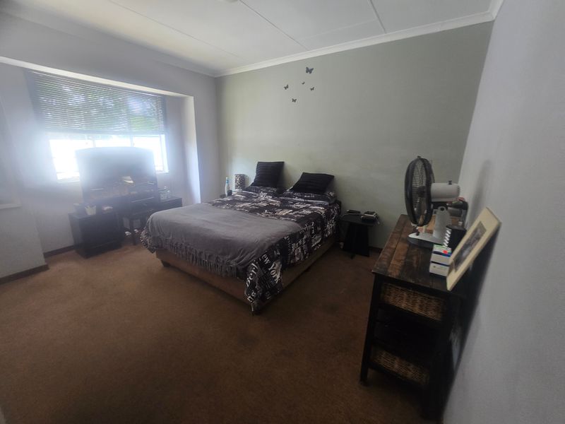 A standard bedroom featuring carpeted flooring, coved ceilings, and a window fitted with venetian blinds.