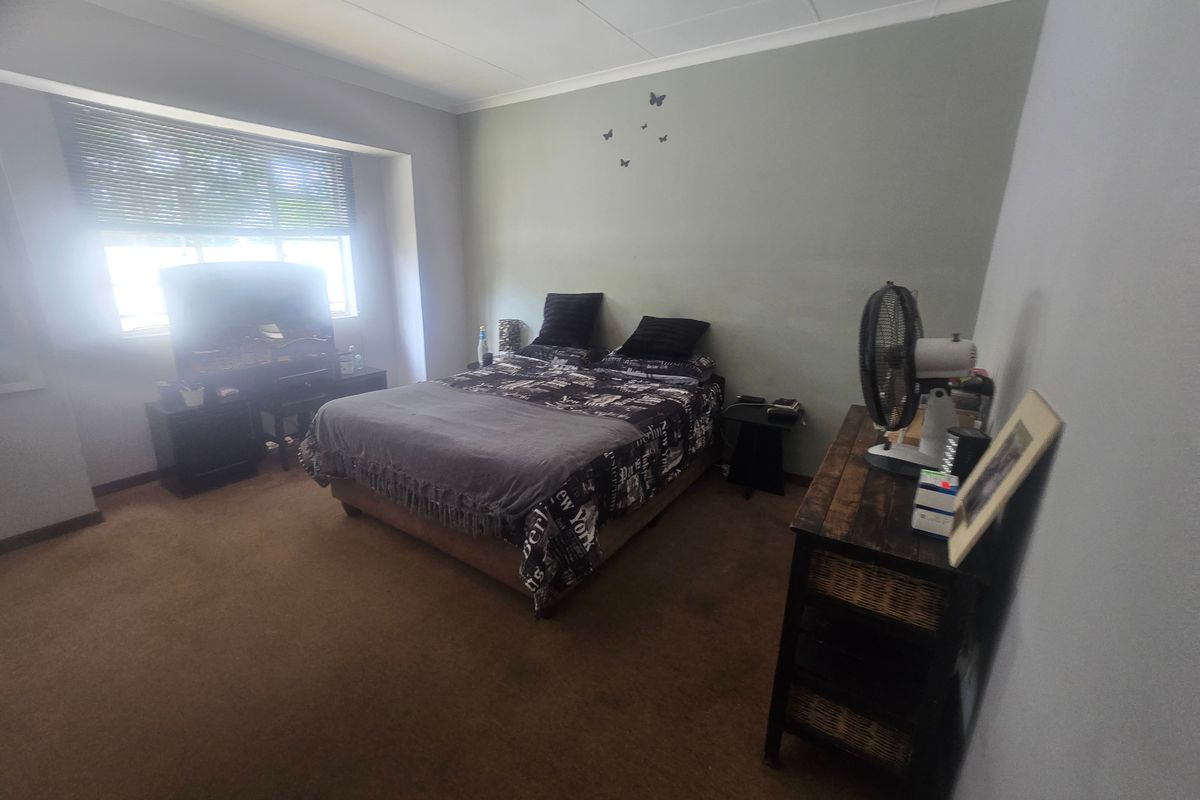 A standard bedroom featuring carpeted flooring, coved ceilings, and a window fitted with venetian blinds.