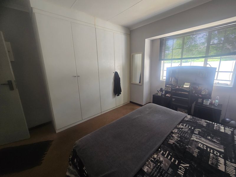 A bedroom featuring built-in cupboards, cove cornicing, and venetian blinds, offering a functional space with potential for cosmetic updates.