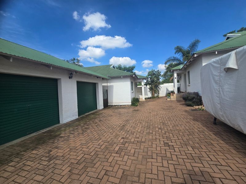 A well-maintained front exterior view featuring a paved driveway, double garage with roller doors, and a clean brick facade under a green metal roof.
