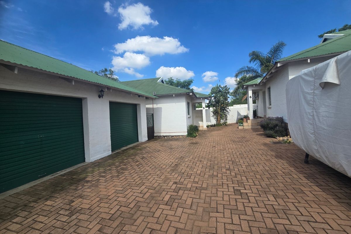 A well-maintained front exterior view featuring a paved driveway, double garage with roller doors, and a clean brick facade under a green metal roof.