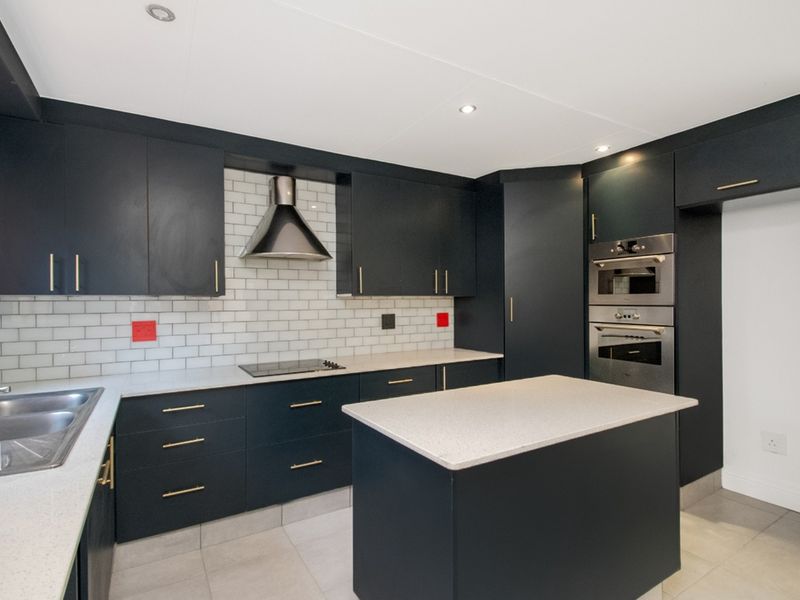 Modern kitchen featuring dark cabinetry, stone countertops, subway tile backsplash, a central island, and integrated stainless steel appliances.