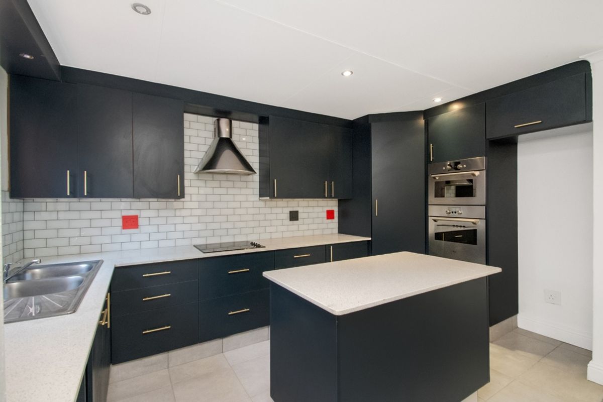 Modern kitchen featuring dark cabinetry, stone countertops, subway tile backsplash, a central island, and integrated stainless steel appliances.