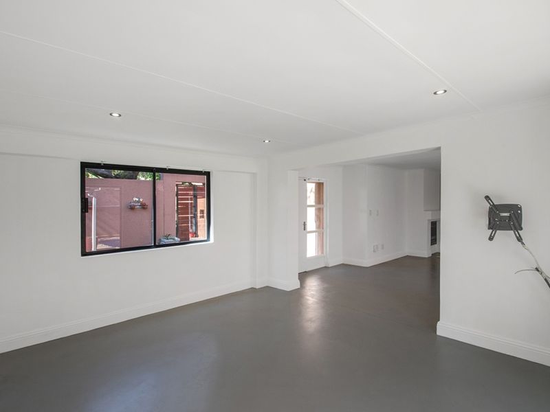 A bright, open-plan living area featuring neutral painted walls, polished concrete flooring, and recessed downlighting, offering a clean and versatile space.