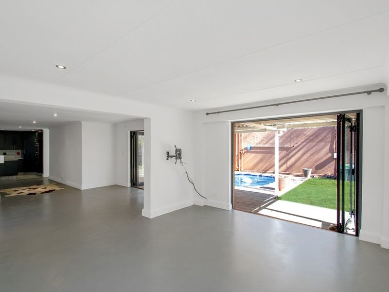 Spacious open-plan living area featuring sleek screeded floors, recessed lighting, and seamless bi-fold doors opening to a private garden and pool area.