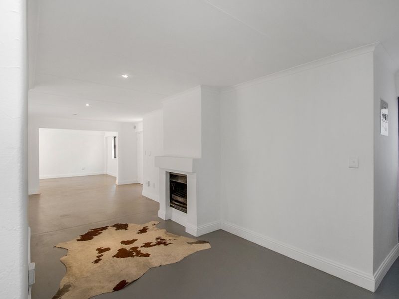 A bright, open-plan living area featuring a built-in fireplace, neutral white walls, and modern screeded flooring throughout.