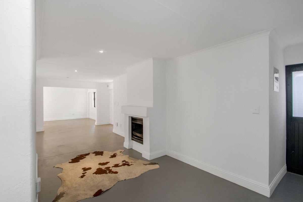 A bright, open-plan living area featuring a built-in fireplace, neutral white walls, and modern screeded flooring throughout.