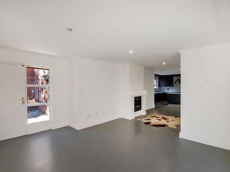 Spacious open-plan living area featuring a fireplace, modern screeded flooring, and direct access to an outdoor space, with a view into the kitchen.