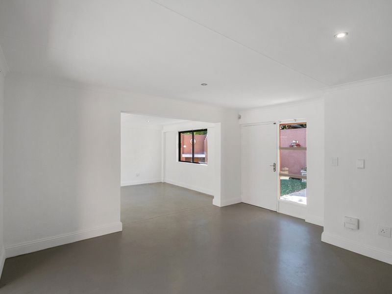 A bright, open-plan living area featuring neutral painted walls, smooth grey flooring, and recessed lighting, offering a versatile space for modern living.