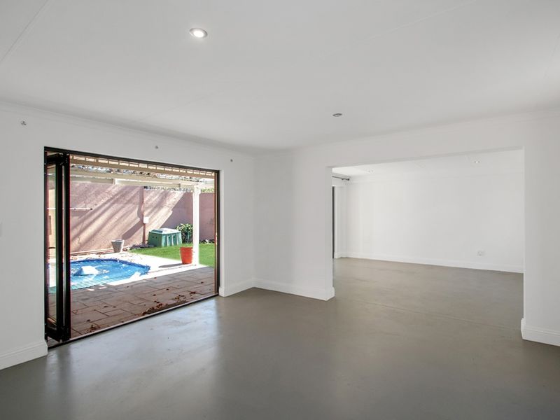 Spacious open-plan living area featuring sleek screeded concrete floors, recessed downlights, and large bi-fold doors opening onto the pool and patio area.