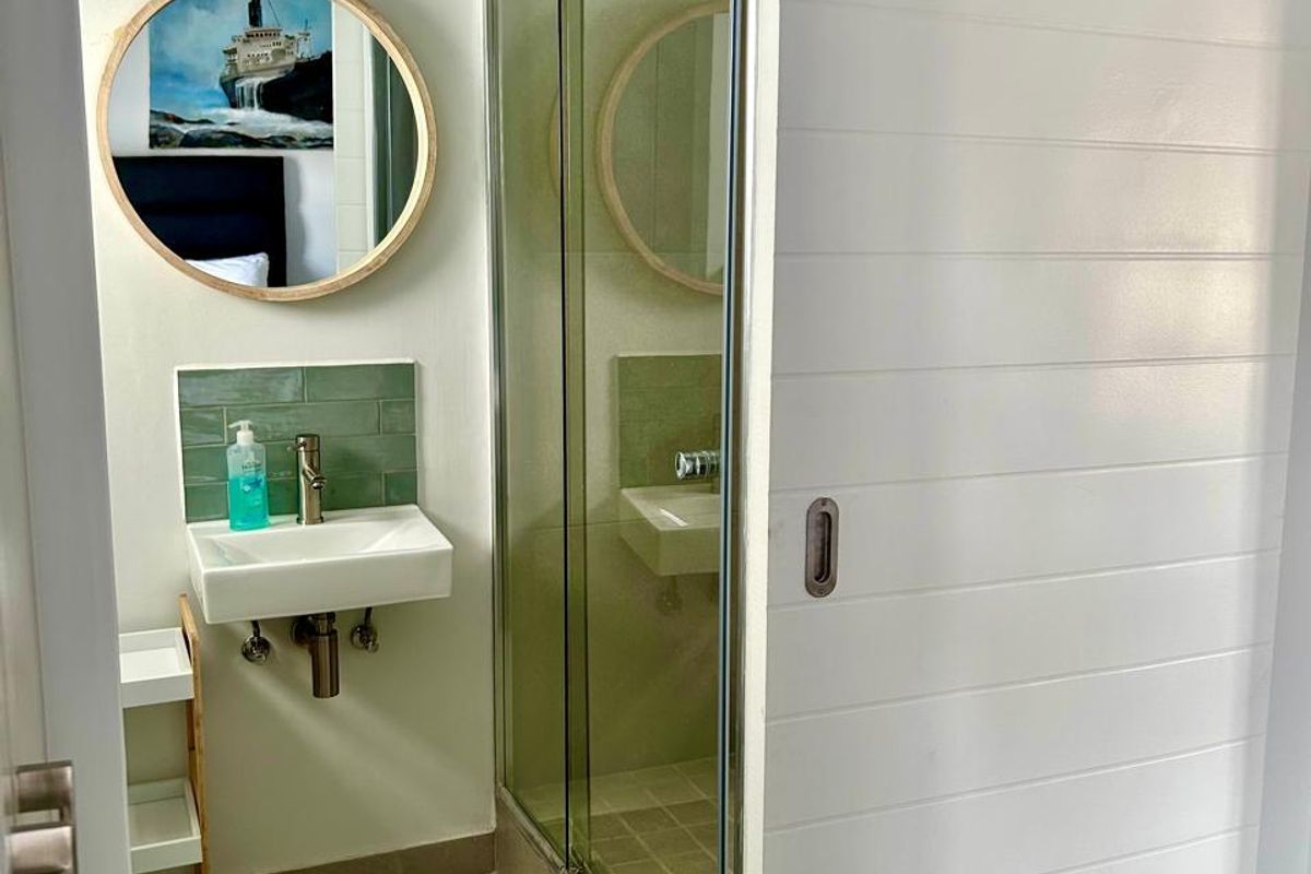 Compact modern bathroom featuring a wall-mounted basin with tiled splashback, chrome fixtures, and a glass-enclosed shower, accessed via a white sliding door.