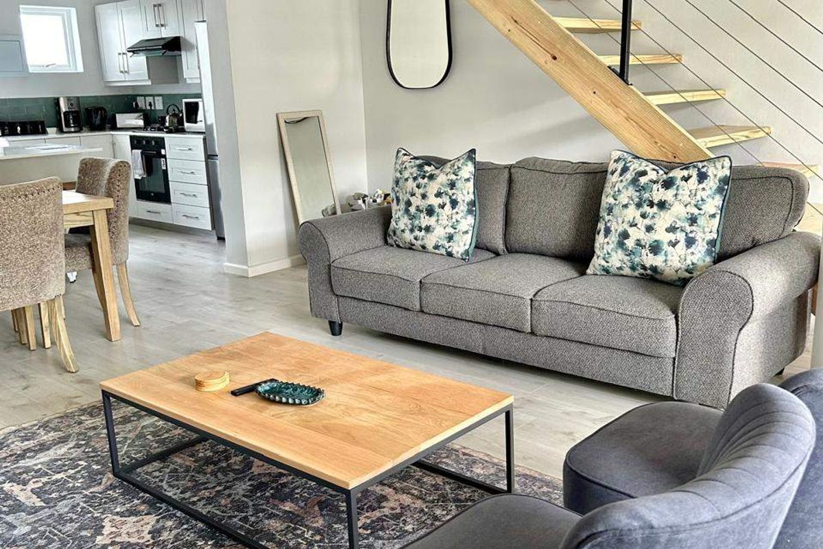 Open-plan living area featuring a modern open-tread staircase with steel balustrades, flowing into a functional kitchen with fitted cabinetry and built-in appliances.