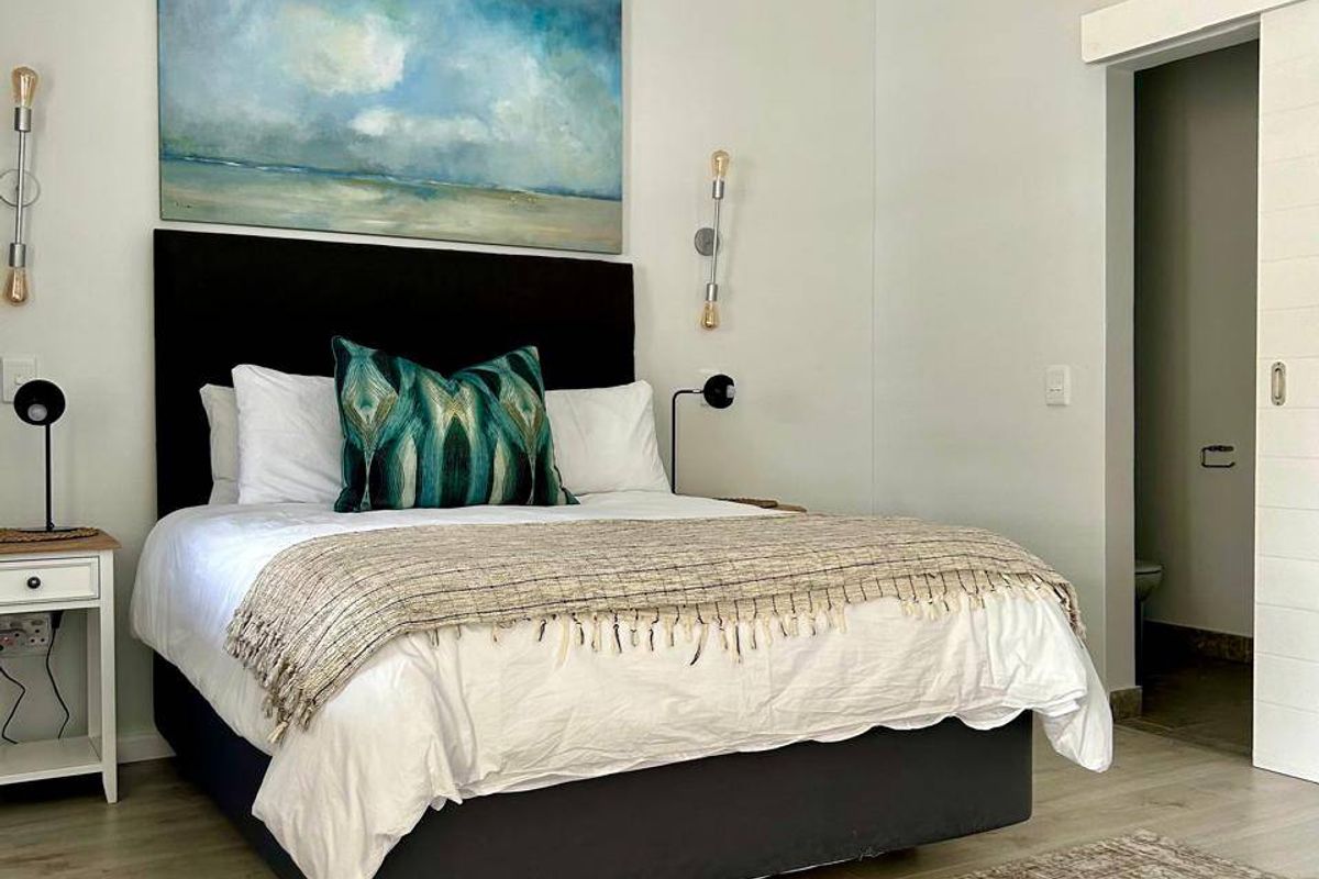 A well-maintained bedroom featuring light laminate flooring, a modern sliding barn door leading to an en-suite, and neutral wall finishes.