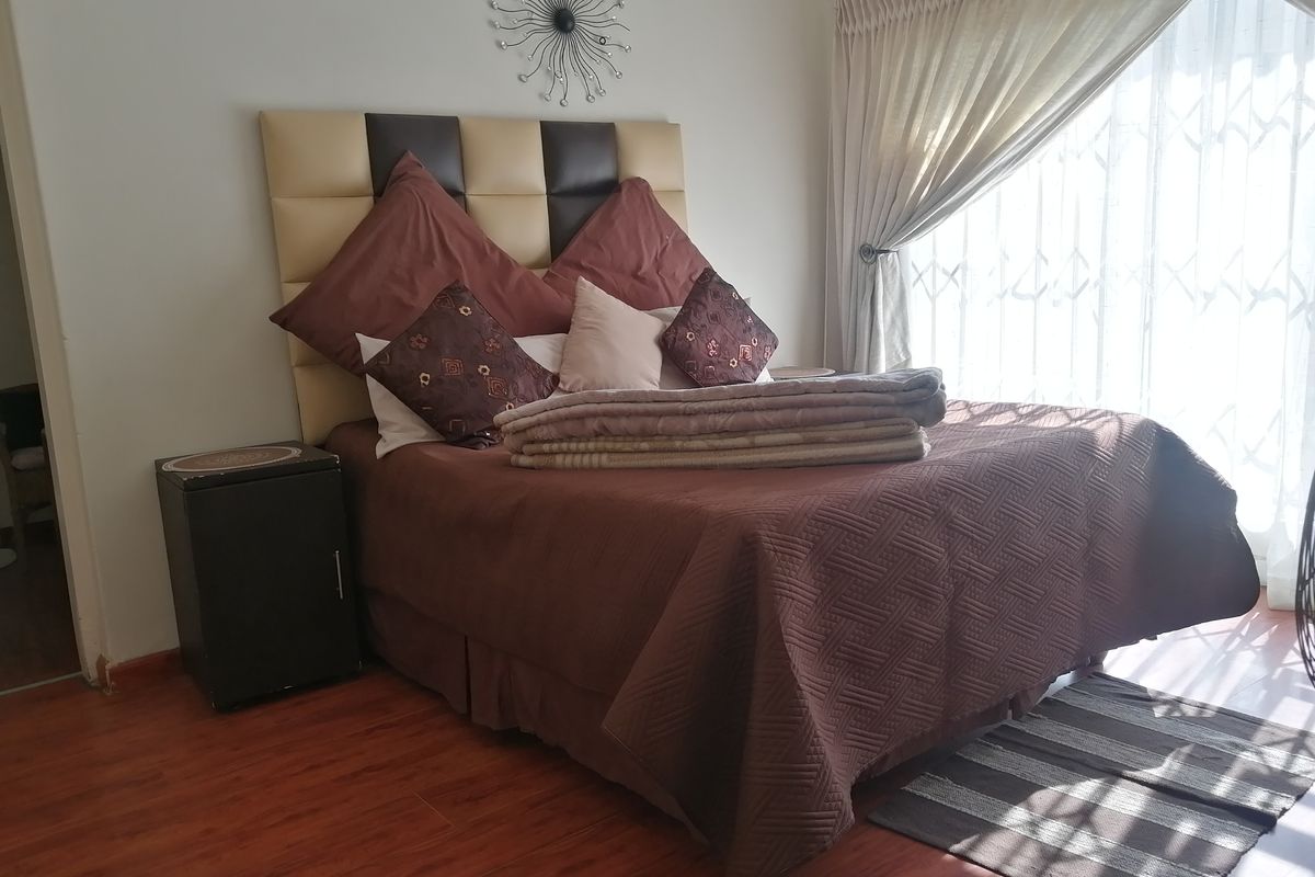 A bedroom featuring laminate flooring and a window fitted with a security gate, providing natural light and essential security.