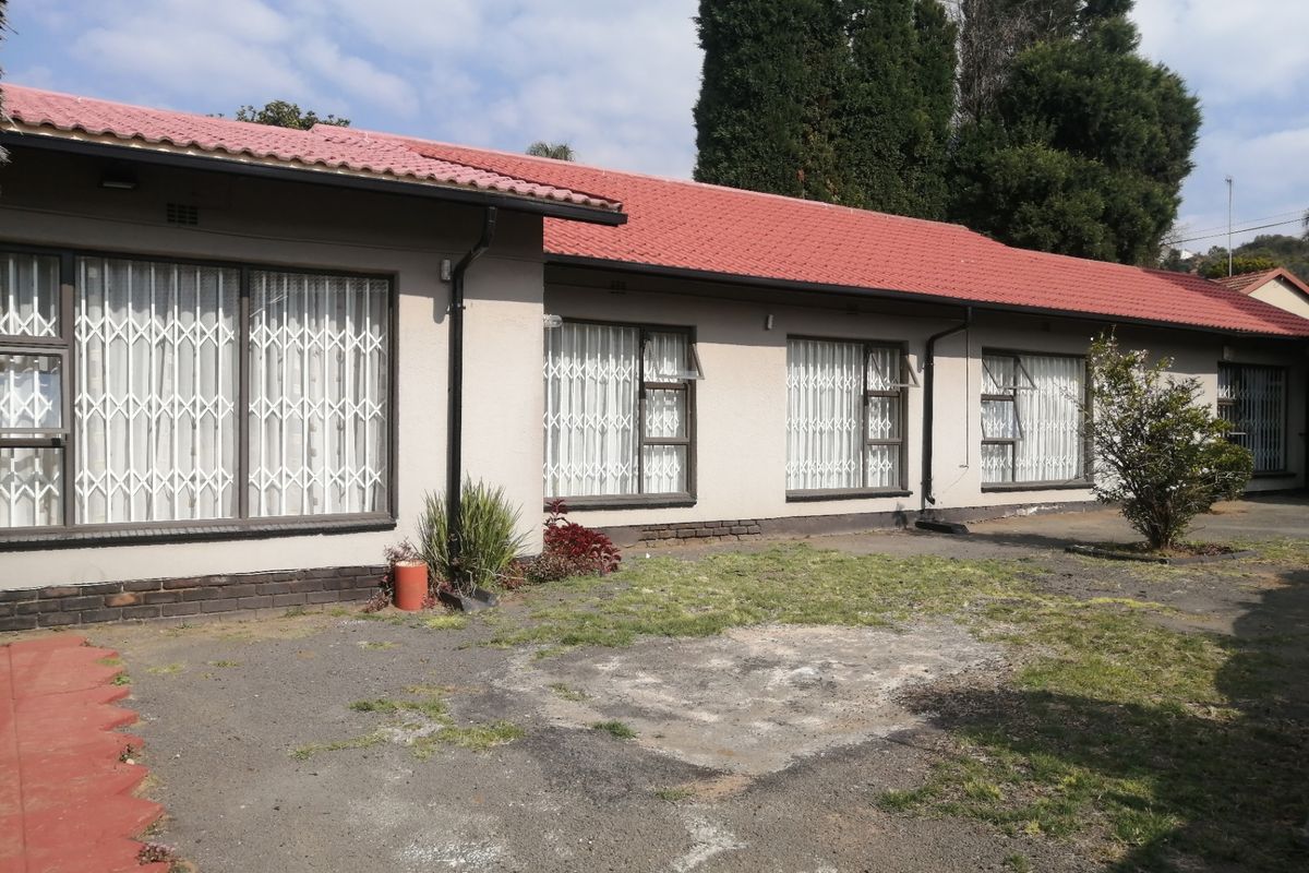 Rear view of the house featuring a red tiled roof, plastered exterior walls, and security gates on the windows, overlooking a paved and lawned area.