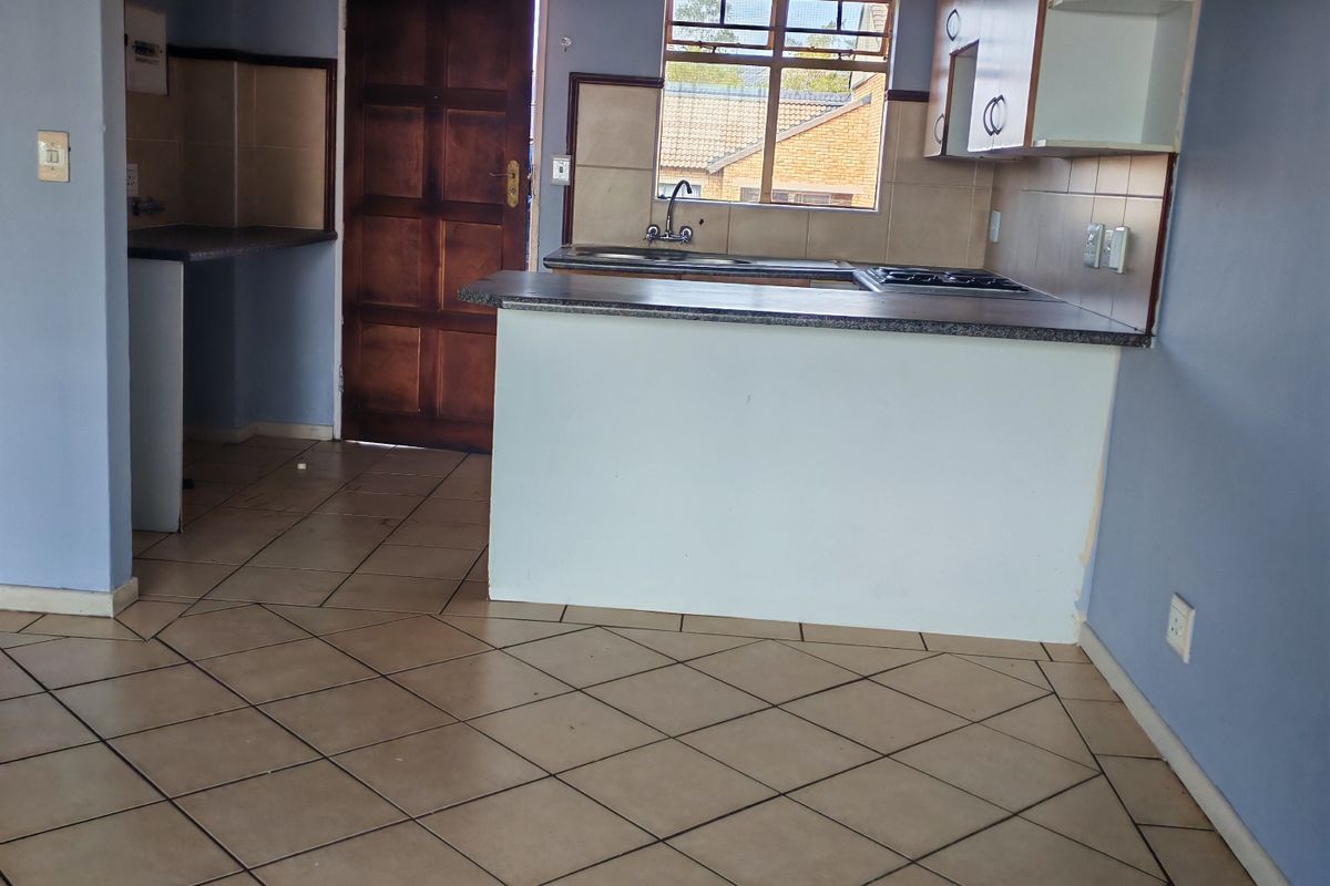 An empty kitchen featuring built-in cabinetry, laminate countertops, a stainless steel sink, and tiled flooring, offering a blank canvas for potential renovation.