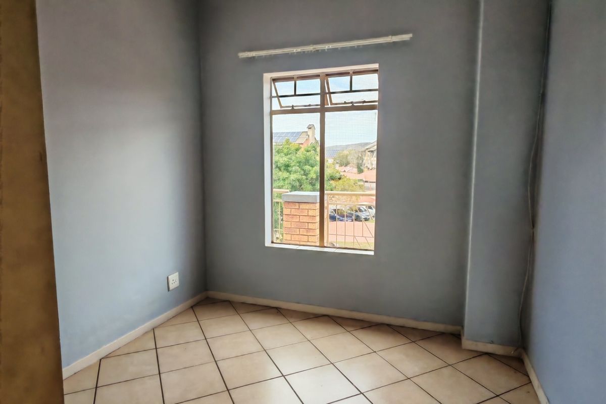 An empty bedroom featuring tiled flooring, neutral blue walls, and a window providing natural light and exterior views.