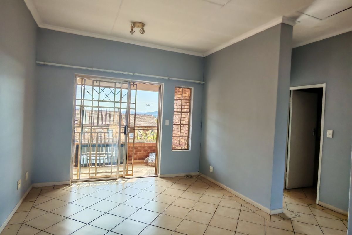 An empty living room featuring tiled flooring, a sliding glass door with security gate, and access to an outdoor balcony area.