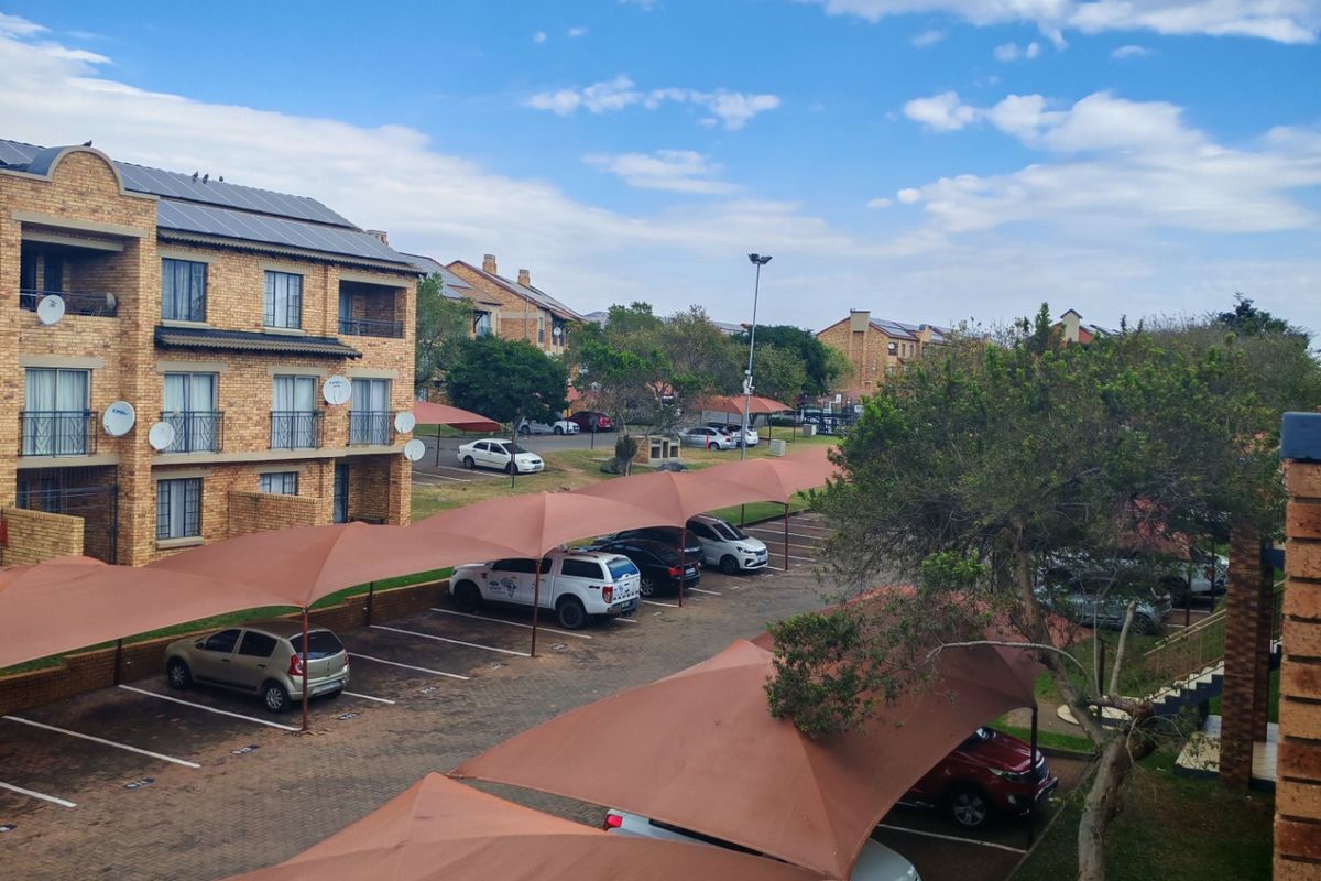 View of the apartment complex parking area featuring paved bays with shade sail coverings and established garden surroundings.