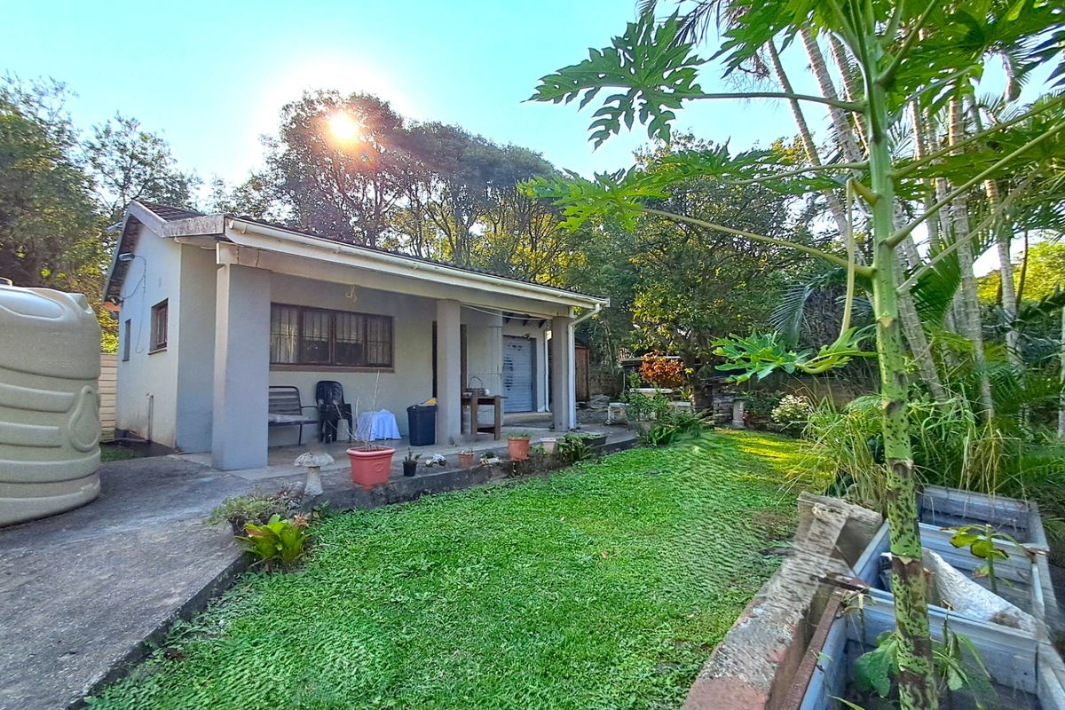 Rear view of the house featuring a covered patio, concrete driveway, water storage tank, and a landscaped garden with raised planting beds.