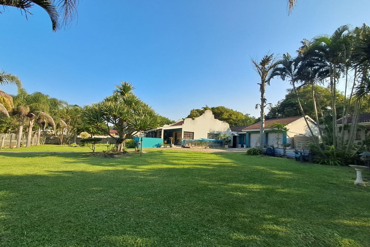 A spacious rear garden featuring a large lawn, mature landscaping, and a view of the main house structure with an attached garage.