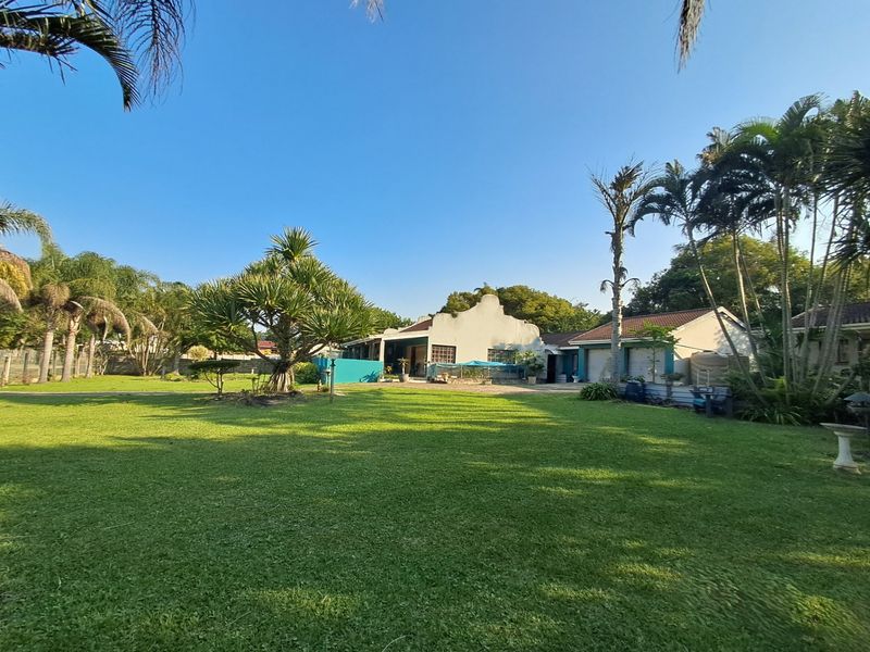 A spacious rear garden featuring a large lawn, mature landscaping, and a view of the main house structure with an attached garage.