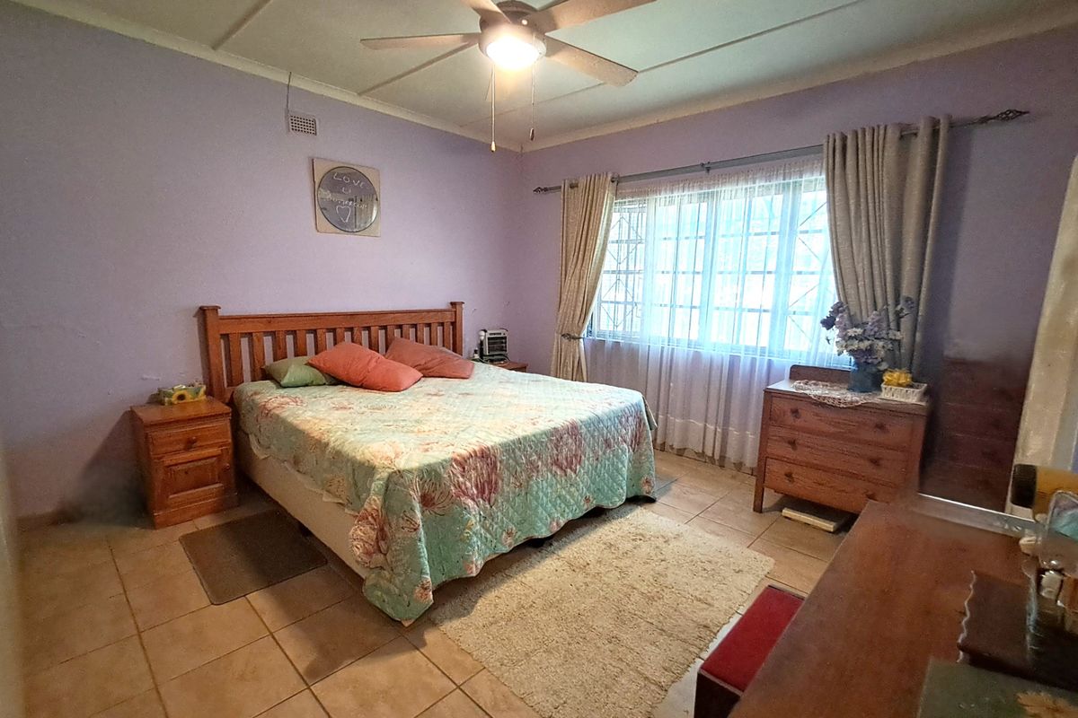 A spacious bedroom featuring tiled flooring, a ceiling fan, and large windows with security bars, offering a functional layout ready for cosmetic updates.