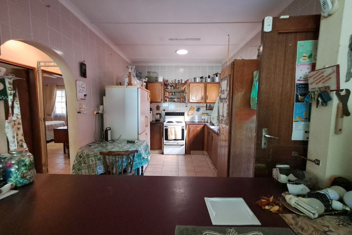 A dated kitchen featuring traditional wooden cabinetry, tiled splashbacks, and a freestanding stove, with an open archway leading to adjacent living spaces.