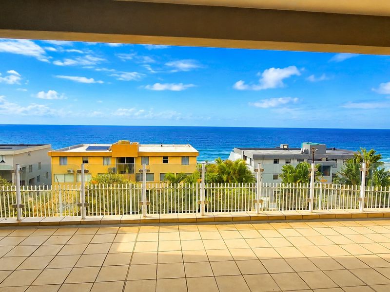 Spacious balcony featuring tiled flooring and a glass balustrade, offering expansive ocean and coastal views.