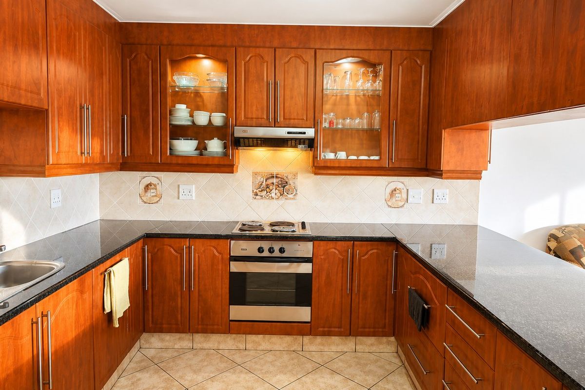 A functional U-shaped kitchen featuring warm-toned wooden cabinetry, granite countertops, a built-in oven with hob, and integrated extractor fan with ample storage space.