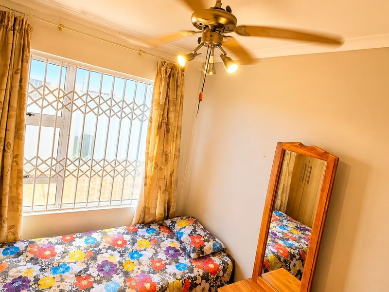 A functional bedroom featuring a built-in wardrobe, ceiling fan, and a window fitted with a security gate.