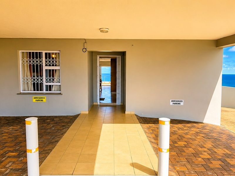 Covered entrance area featuring a paved driveway, tiled walkway, and security bars on windows, with a view towards the ocean.