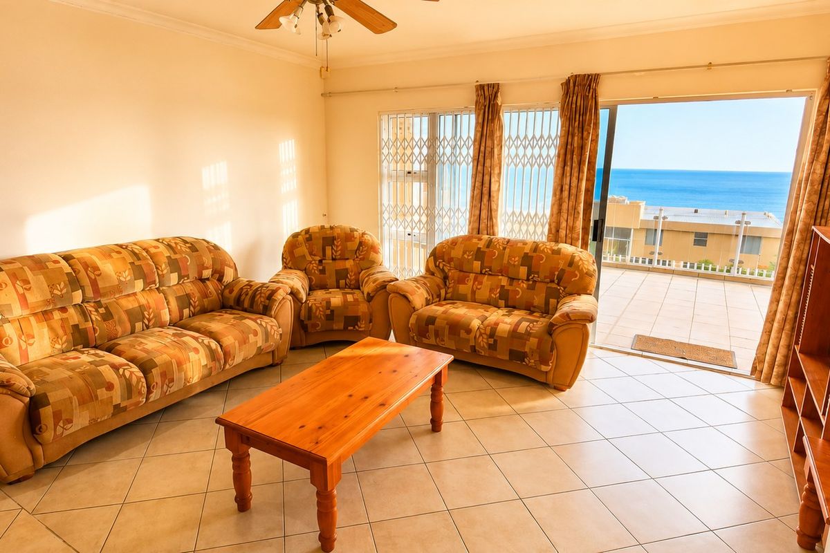 Spacious living room featuring tiled flooring, a ceiling fan, and direct access to a balcony with ocean views.