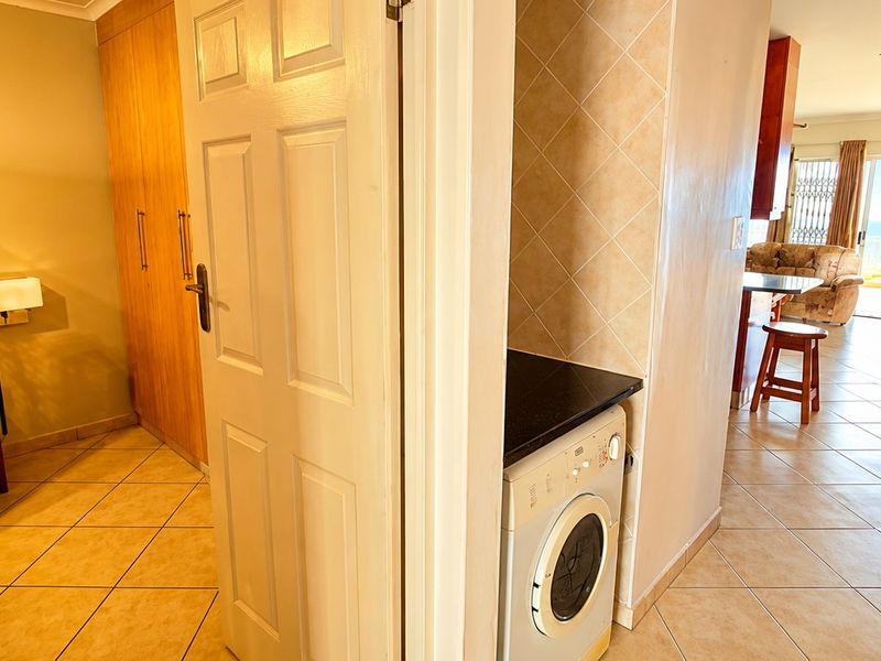 A compact laundry nook featuring built-in cabinetry, a stone countertop, and a washing machine, conveniently located adjacent to the main living area.